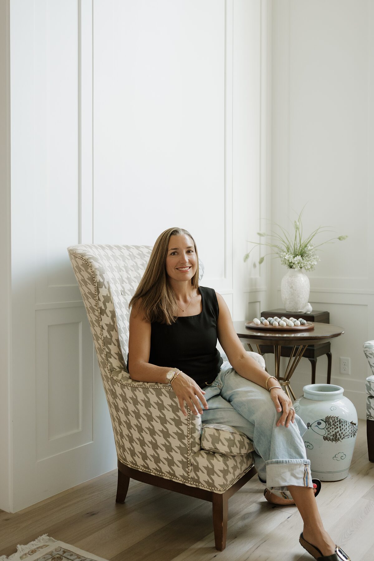 Jacqulynn Michelle seated in a houndstooth wing chair in a bright, paneled room with warm wood floors