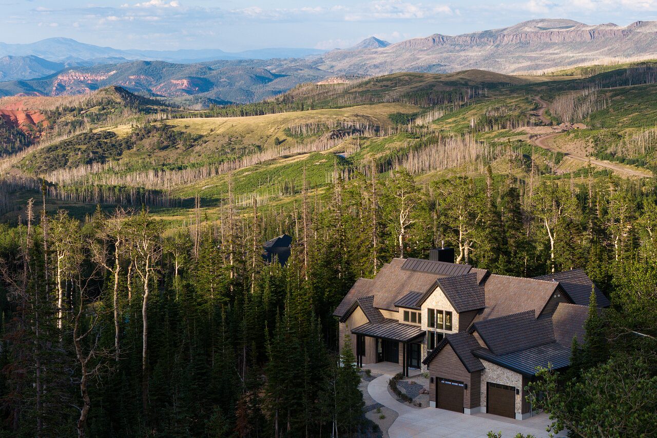 Aerial view of Bluebell Court among aspens and pines, with the Cedar Breaks plateau and red cliffs on the horizon