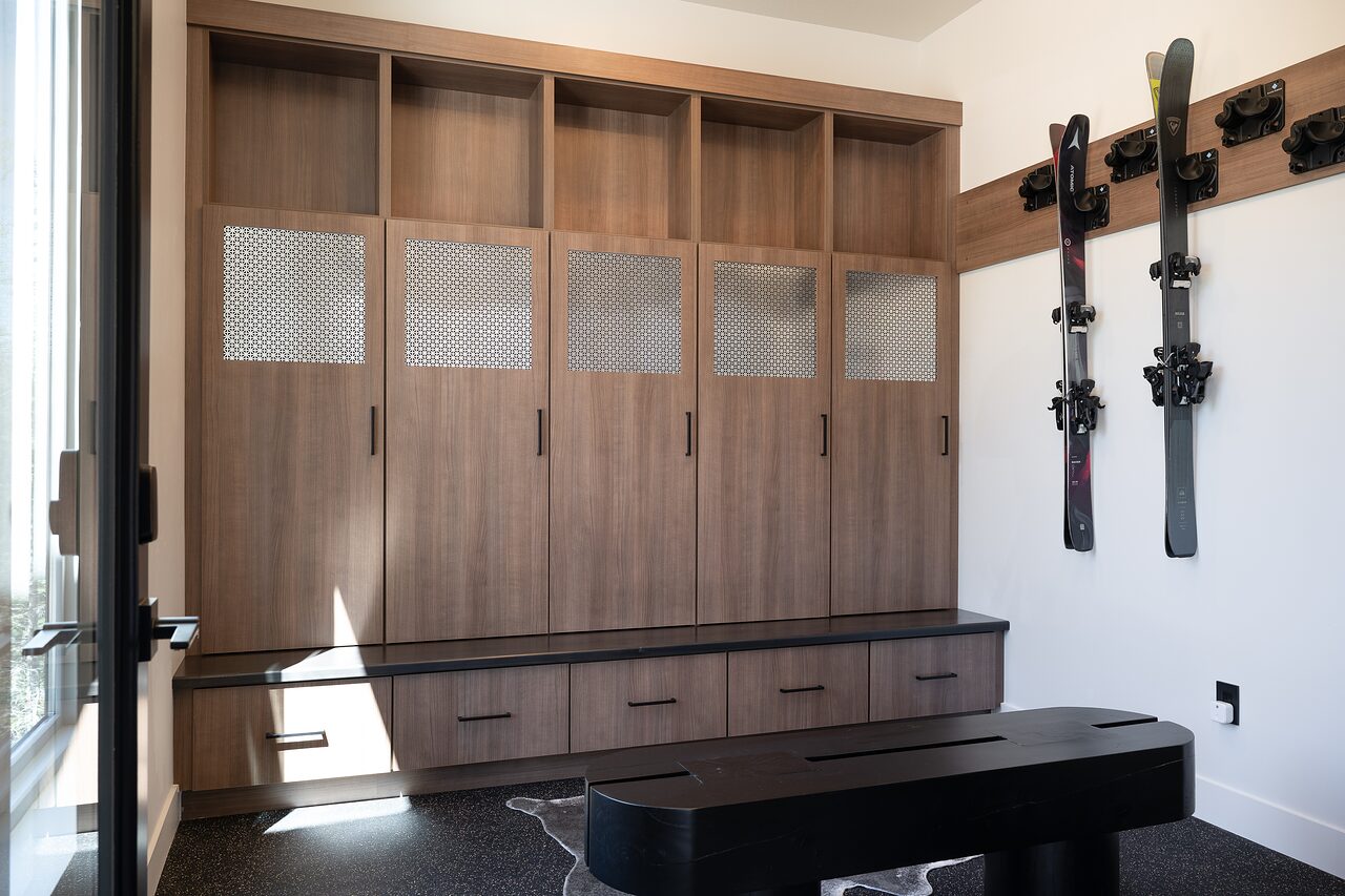 Ski mudroom with warm wood lockers, perforated metal cabinet fronts, a black bench, and wall-mounted skis