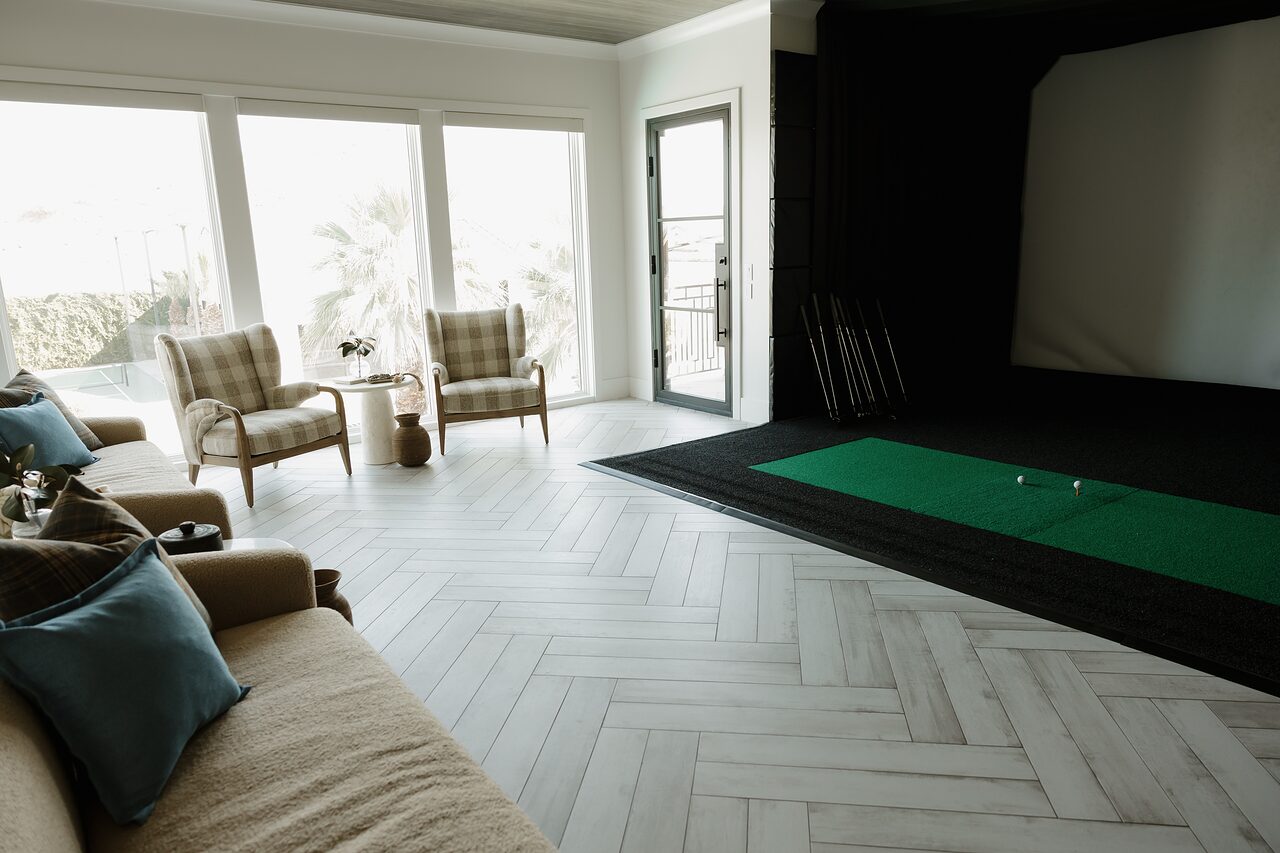 Golf simulator bay with a dark enclosure, projection screen, and green hitting mat beside the lounge seating