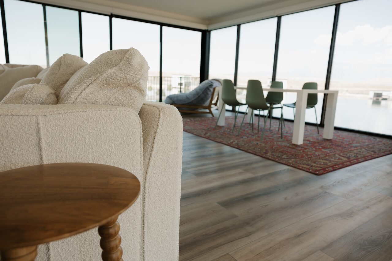 Boucle sectional and a spindle side table in the foreground with the dining table, sage chairs, and a red rug at the glass wall